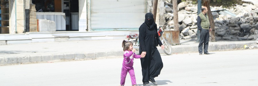 سيدة وطفلتها تقطع الشارع أمام مبنى مهدم في حي المرجة في حلب. تصوير حسام كويفاتية
