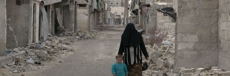 أمرأة تمشي مع طفلها في حارة مهدمة في السكري في حلب. تصوير براء الحلبي