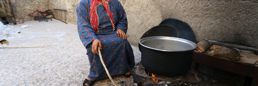 أمرأة نازحة من كوباني الى الشيخ مقصود تطبخ على الحطب. تصوير براء الحلبي
