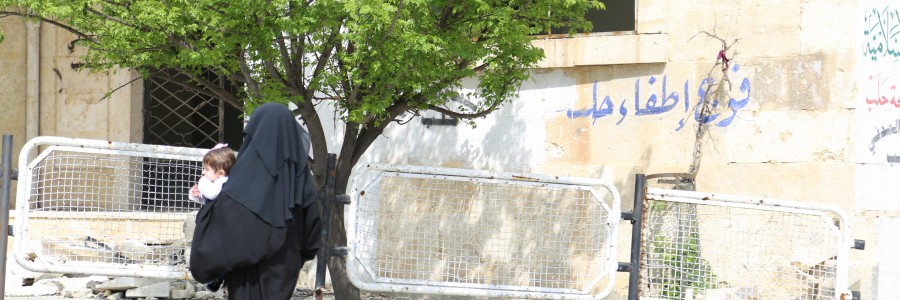 سيدة وطفلها تمشي أمام فوج اطفاء حلب في حي قاضي عسكر. تصوير حسام كويفاتية